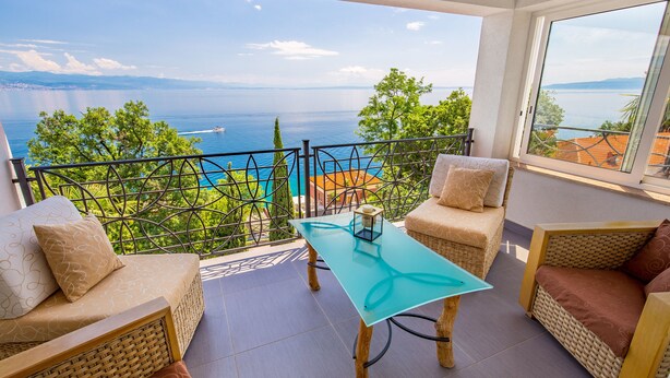 Un balcon agrémenté de meubles en osier, d’une table en verre et offrant une vue sur la mer.