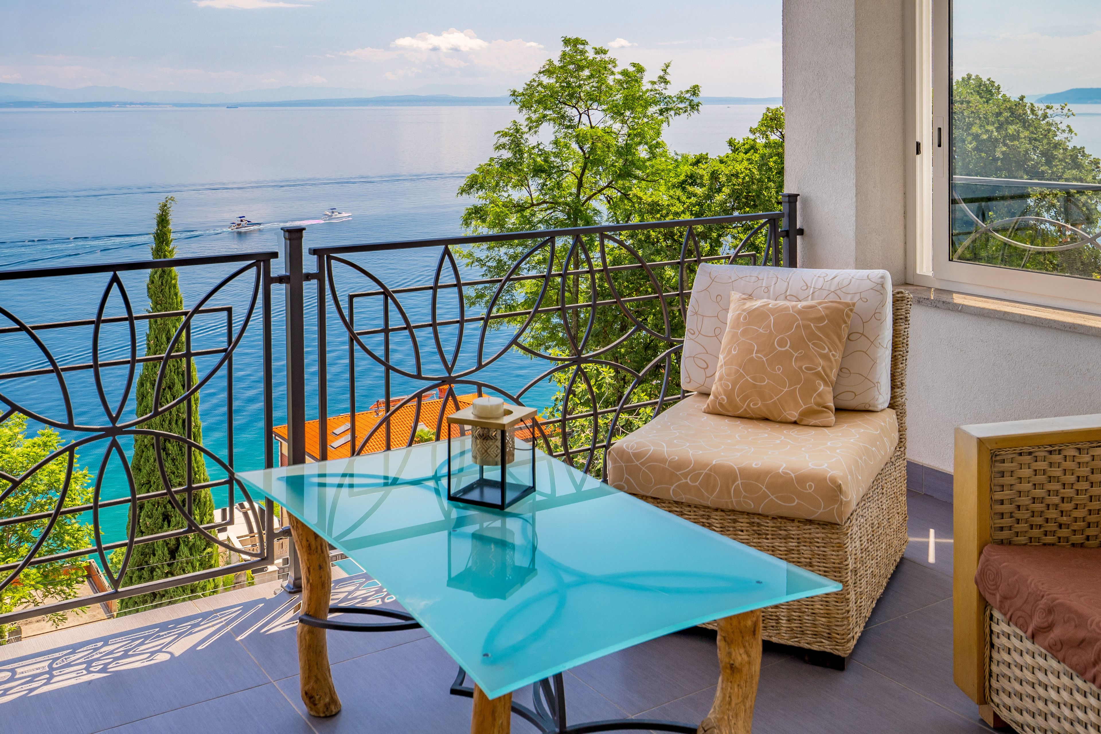 Een balkon met een glazen tafel, rieten meubilair en uitzicht op zee.