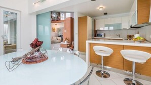 Une cuisine moderne avec des meubles blancs, un îlot central doté de tabourets, et un coin repas avec une table et des chaises en verre.