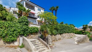 Un bâtiment blanc avec un escalier en pierre menant à un balcon, entouré d’une végétation luxuriante et de palmiers.