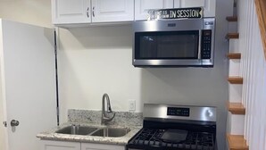 A compact kitchen with white cabinets, a stainless steel stove, a microwave, and a granite countertop sink. - Charming Beach Cottage Duplex-Huge Upper Level  (Newport Beach)