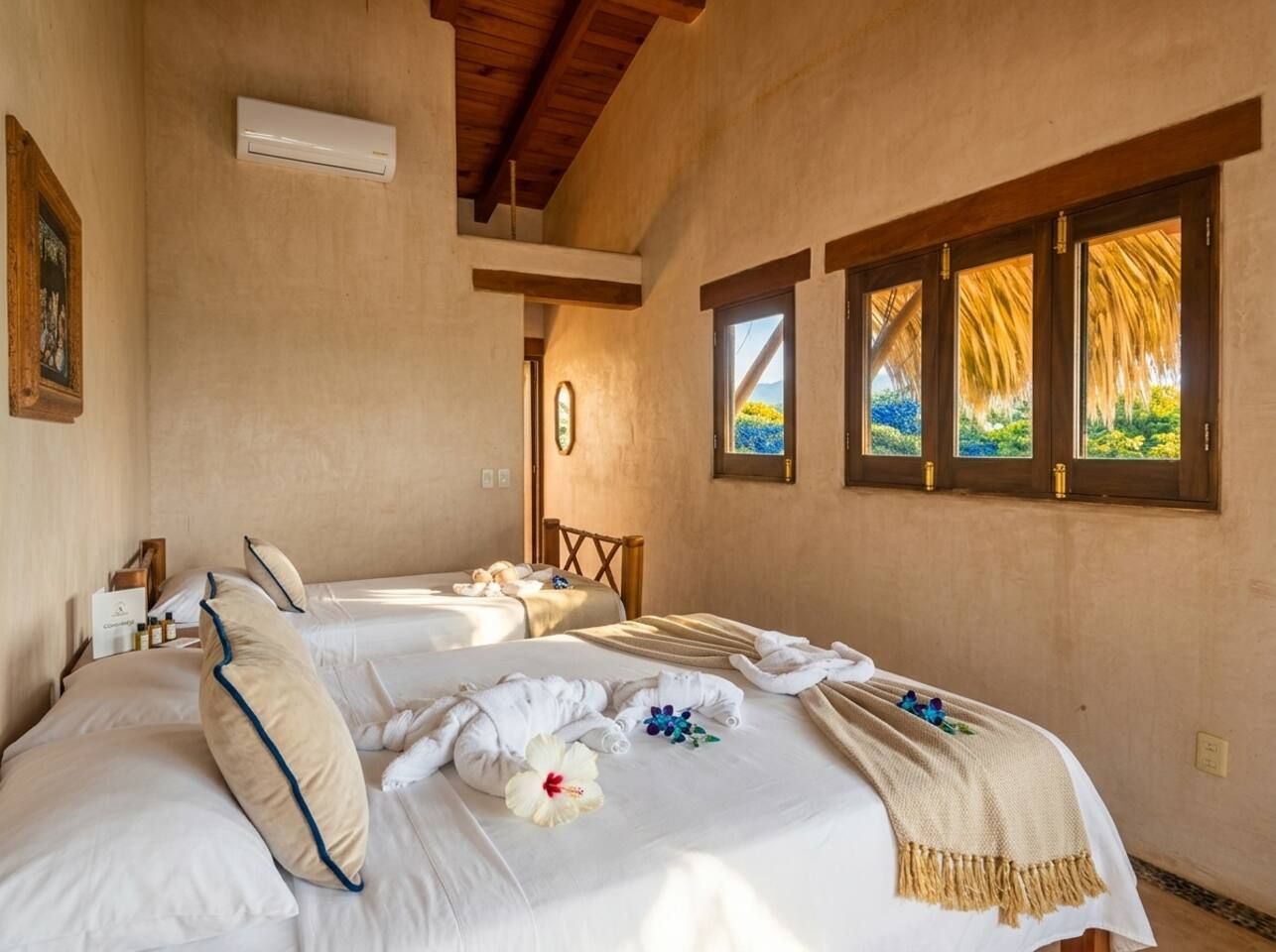 Une chambre d’hôtel avec deux lits, un plafond en bois, une fenêtre donnant sur un beau paysage et un climatiseur fixé au mur.