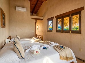 Una habitación de hotel con dos camas, techo de madera, ventana con vistas y aire acondicionado instalado en la pared.