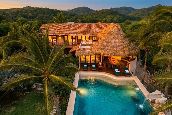 A resort with a swimming pool, thatched-roof structures, and lush greenery.