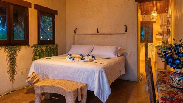 A bedroom with a bed, a small bench, and a window with a view of trees. - Luxury Eco Retreat in Troncones City (Troncones)