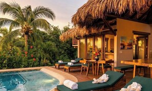 A poolside area with lounge chairs, a dining table, and a thatched-roof structure.