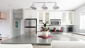 A modern kitchen with white cabinets, stainless steel appliances, and a central island with seating. - Ramsay Manor | Spacious 1BR Queen Bed Inner City (Calgary)