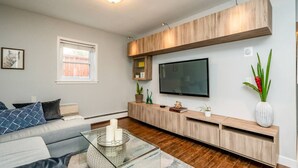 A modern living room with a sofa, coffee table, TV, and built-in wooden shelves. - Ramsay Manor | Spacious 1BR Queen Bed Inner City (Calgary)