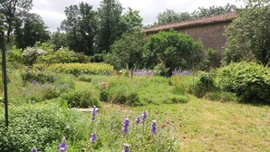 A garden with various flowers and trees, a brick building, and a wooden fence. - Gite du potager, Gite 2 to 5 bedrooms (Azay-le-Brûlé)