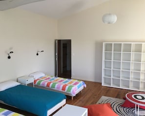 Une chambre avec deux lits, une armoire blanche, une petite table et un luminaire suspendu.