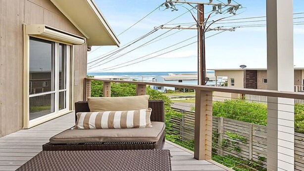 A balcony with a sofa, a window, and a view of the sea. - 11 Hero Ave - Spacious Family Home, with spectacular ocean and hillside views, right near the beach (Middleton)