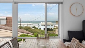A room with a large sliding glass door leading to a balcony with a view of the sea and other buildings. - 11 Hero Ave - Spacious Family Home, with spectacular ocean and hillside views, right near the beach (Middleton)