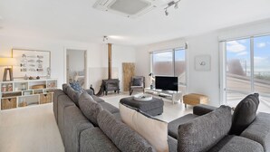 A modern living room with a sofa, television, and a fireplace. - 11 Hero Ave - Spacious Family Home, with spectacular ocean and hillside views, right near the beach (Middleton)