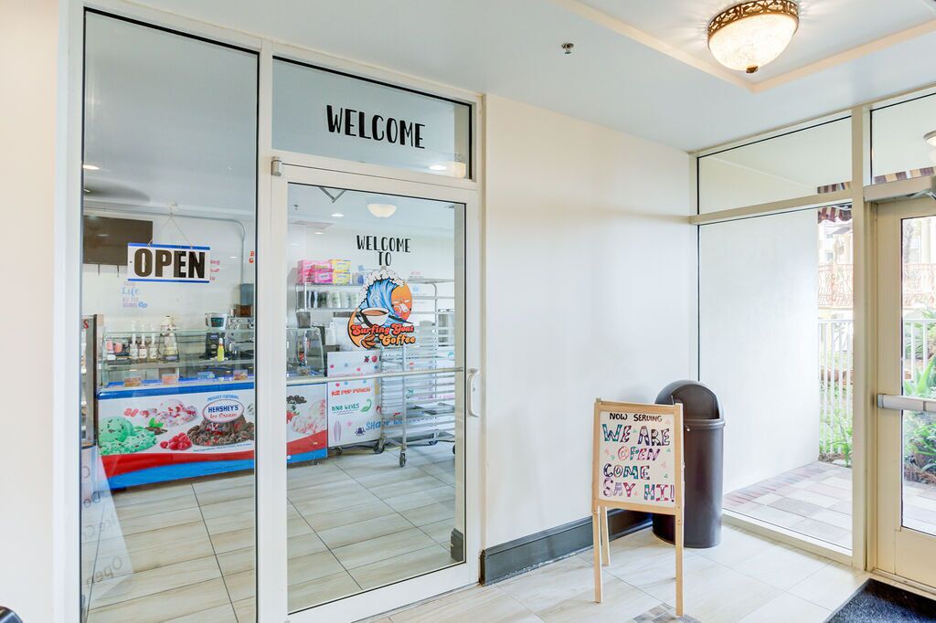Un rètol de cristalleria amb un cartell de 'WELCOME', un cartell de 'OPEN' i un panell publicitari que anuncia 'Sizzling Sun & Coffee'.