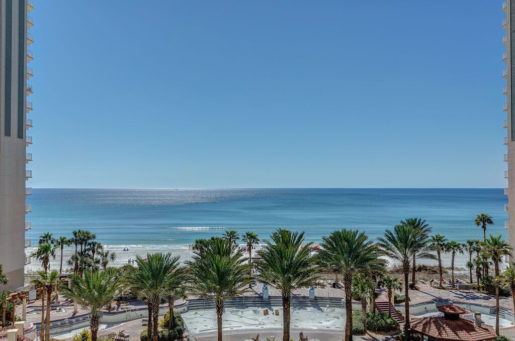 A beach view from a balcony with palm trees and a clear blue sky.