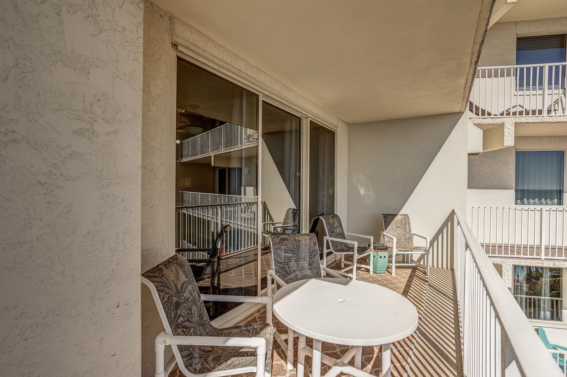 A balcony with a white table and chairs, a staircase, and a view of the building's interior.