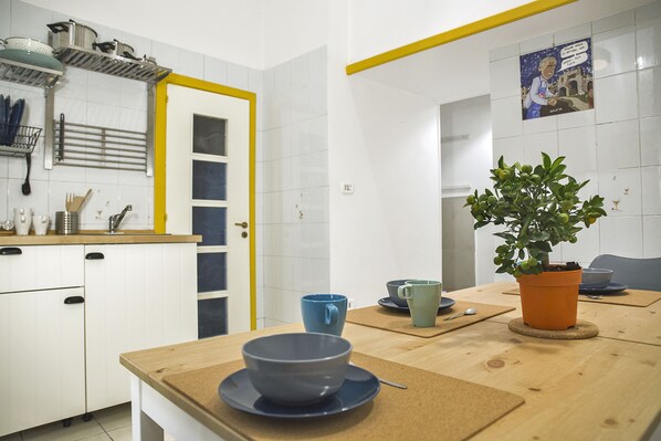 A kitchen with white cabinets, a yellow door frame, a potted plant, and a table with a blue bowl and spoon.