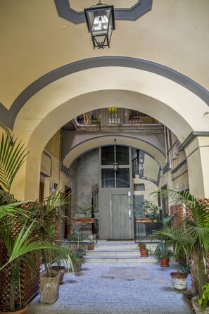 An arched entrance with potted plants, a wooden door, and a balcony with railings.