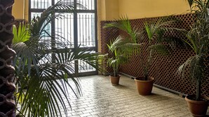 A hallway with a tiled floor, potted plants, a large arched window, and a ceiling light fixture. - 26 Urban Guest House (Naples)