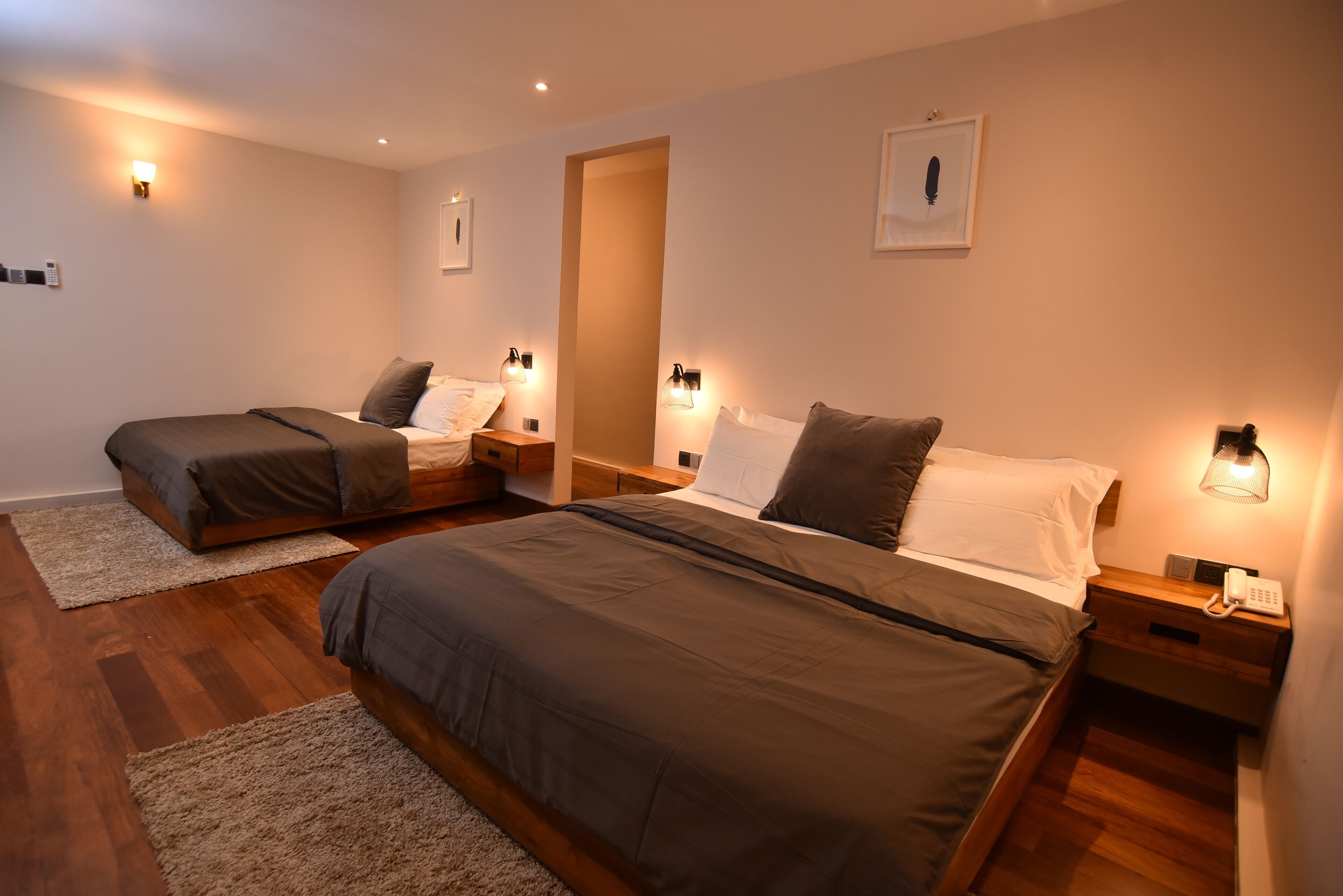 A hotel room with two single beds, wooden flooring, and bedside lamps.
