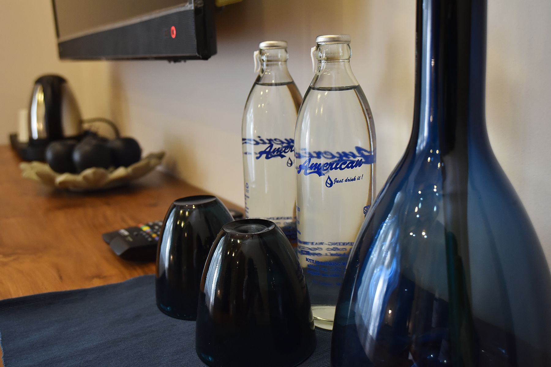 Una mesa con tres botellas de agua American, un florero negro y una tetera negra.