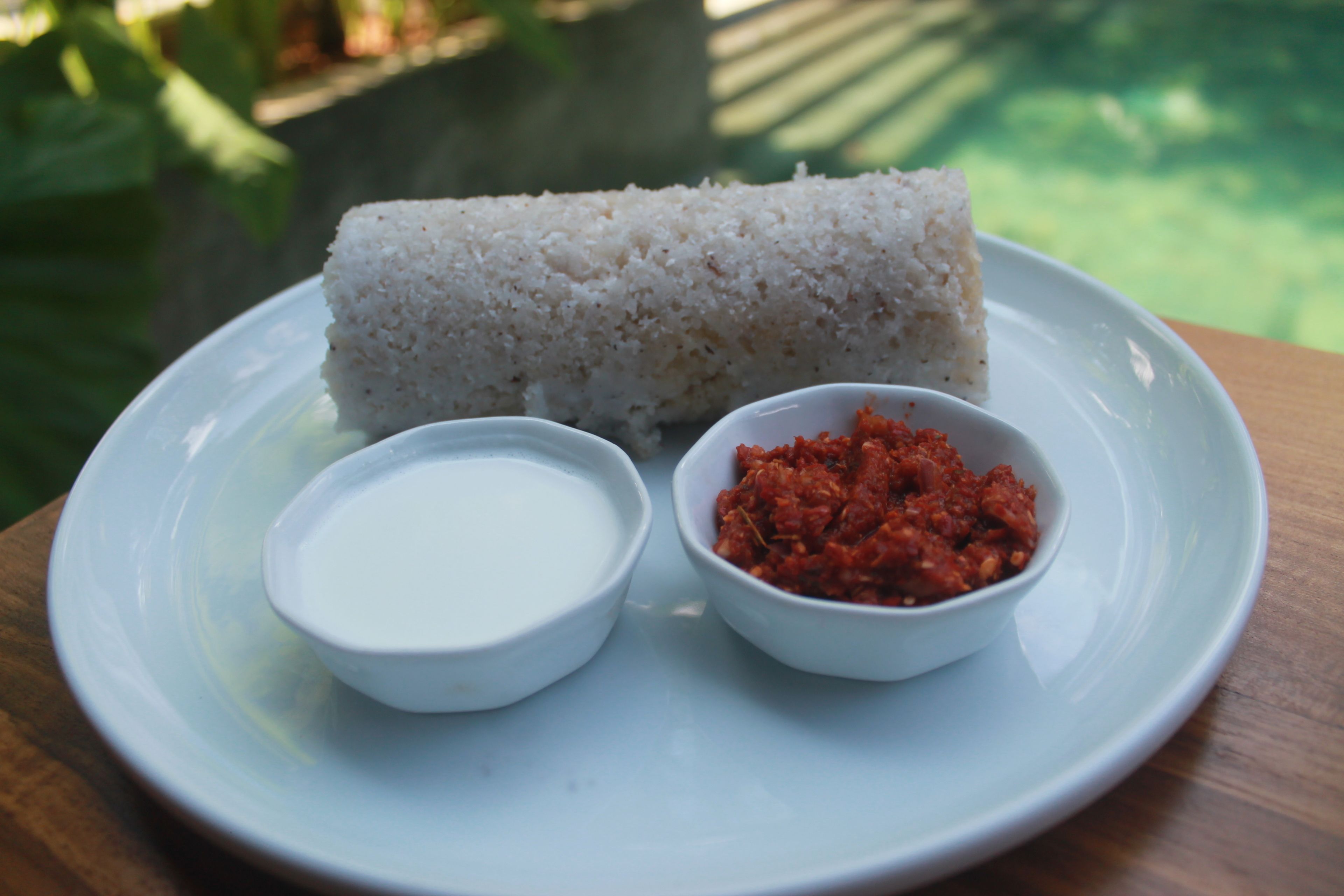 A plate with a white rice roll, a small bowl of white sauce, and a small bowl of red sauce.