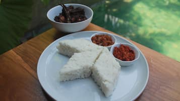 A plate of white rice with three sides, two small bowls of red sauce, and a bowl of dark-colored food on a wooden table.