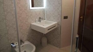 A bathroom with a glass shower enclosure, a pedestal sink, and a toilet.