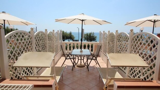 An outdoor seating area with tables and chairs, surrounded by white lattice panels, and overlooking a body of water.