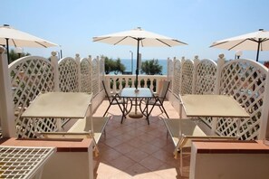 An outdoor seating area with tables and chairs, surrounded by white lattice panels, and overlooking a body of water. - Del Prado monolocale 109 (Riva Ligure)