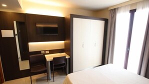 A hotel room with a bed, a desk, a chair, a TV mounted on the wall, and a wardrobe.
