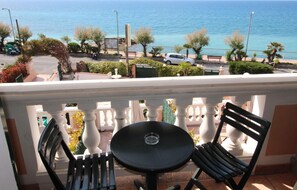A balcony with a table and chairs overlooking a coastal area with parked cars and trees. - Del Prado monolocale 214 (RIVA LIGURE)