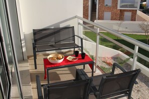 A balcony with a table set for breakfast, including a bowl of cereal, a plate, and cups.