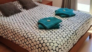 A neatly made bed with a patterned bedspread, two pillows, and folded towels on a wooden headboard. - Beautiful new apartment with swimming pool on the Portuguese Silver Coast (Salir do Porto)