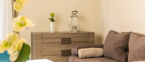 Een woonkamer met een beige bank, een houten bijzettafeltje met een bloemenvaas en een metalen lantaarn.