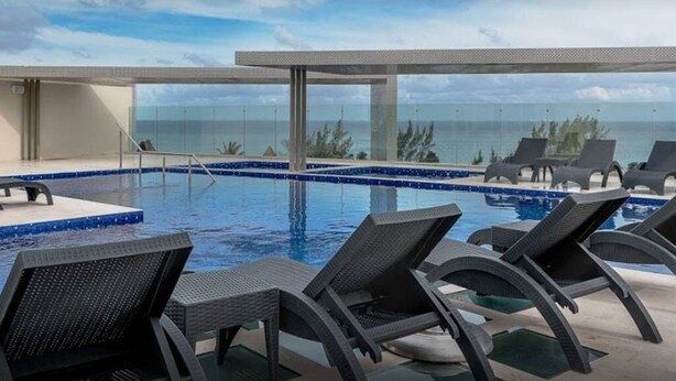 A pool area with lounge chairs and a view of the ocean. - New condo in best building Playa, 1 block from beach, amazing rooftop pool (Zazil-ha)