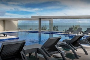 A pool area with lounge chairs and a view of the ocean. - New condo in best building Playa, 1 block from beach, amazing rooftop pool (Zazil-ha)