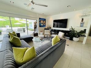 A modern living room with a large grey sofa, a glass coffee table, and a flat-screen TV mounted on the wall.
