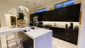 A modern kitchen with dark cabinets, a marble countertop, and stainless steel appliances. - Warm Sands Mid-Century Oasis (Palm Springs)