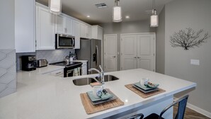 Una cucina moderna con mobili bianchi, elettrodomestici in acciaio inossidabile e illuminazione a sospensione.