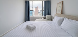 Une chambre d’hôtel avec un lit, une fenêtre avec des rideaux, une vue sur la ville et une œuvre d’art encadrée au mur.