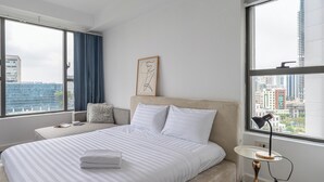 Una habitación de hotel moderna con una cama grande, una mesita de noche, una lámpara y vistas a la ciudad.