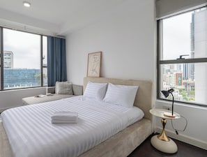 Une chambre dâhĂŽtel moderne avec un grand lit, une table de chevet, une lampe et une vue sur le paysage urbain.