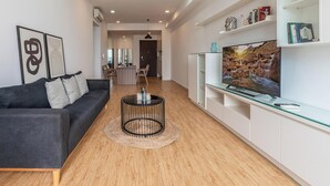 Una sala de estar moderna con un sofá negro, una mesa de centro, un televisor y una estantería.