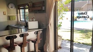 Un espacio habitable compacto con kitchenette, comedor con mesa y sillas, y un amplio ventanal corredero que da a un área exterior.