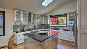 A modern kitchen with a central island, stainless steel appliances, and a window with a view of greenery. - AMAZING, OCEAN VIEWS,
MORRO 🪨, JACUZZI, WIFI, PARKING (Morro Bay)