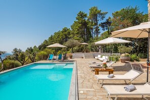 A pool area with lounge chairs and umbrellas, surrounded by trees and a stone patio. - Exclusive Villa, A / C, Pool, Sauna, Gym, Beach Volleyball, Free Wi-Fi, Sat TV, BBQ (Sarzana)