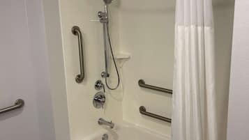 Un baño moderno con ducha a nivel, barras de apoyo y una bañera blanca.