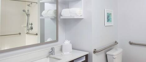 A modern bathroom with a white sink, a large mirror, a toilet with grab bars, and shelves with towels.