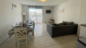 Uma sala de estar com área de jantar, sofá, TV e varanda com cortinas.